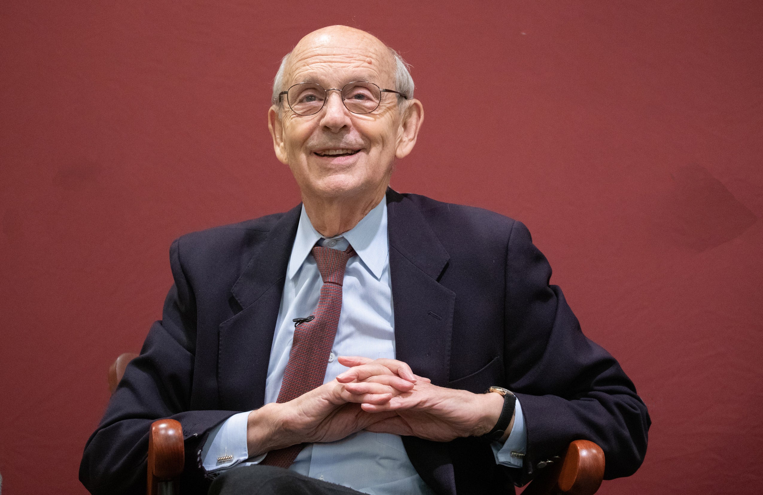 Justice Stephen G. Breyer sitting in a chair in front of a crimson background
