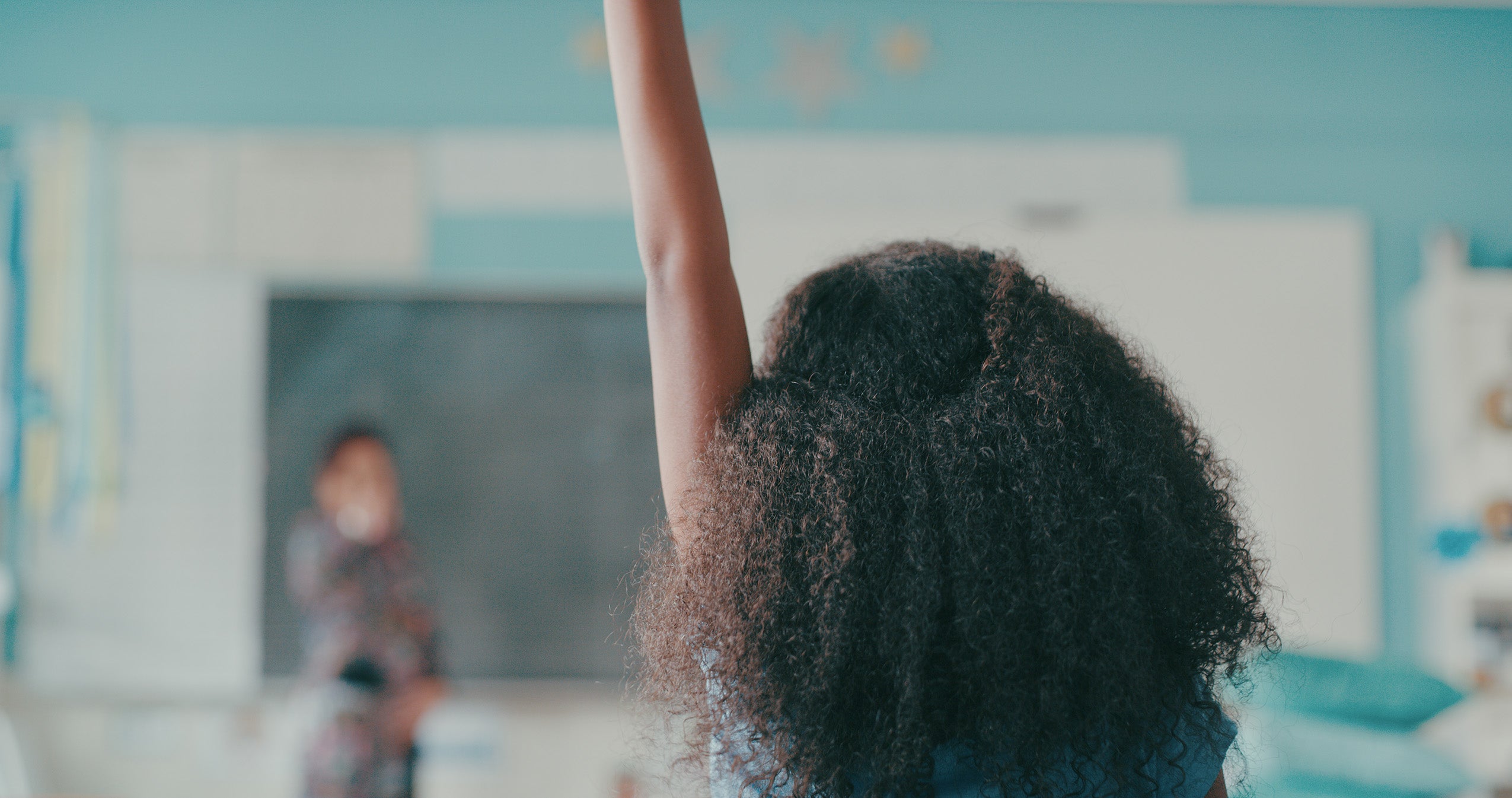 A girl enthusiastically raises her hand in a classroom.