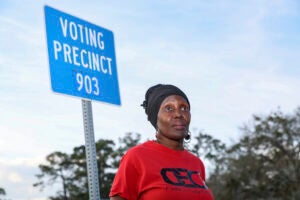 Voting rights activist Rosemary McCoy stands in front of a blue sign that reads 